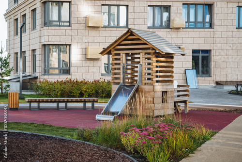 There is a charming wooden playground that features a slide prominently positioned in front of a wellstructured building, creating a delightful scene for children to enjoy photo
