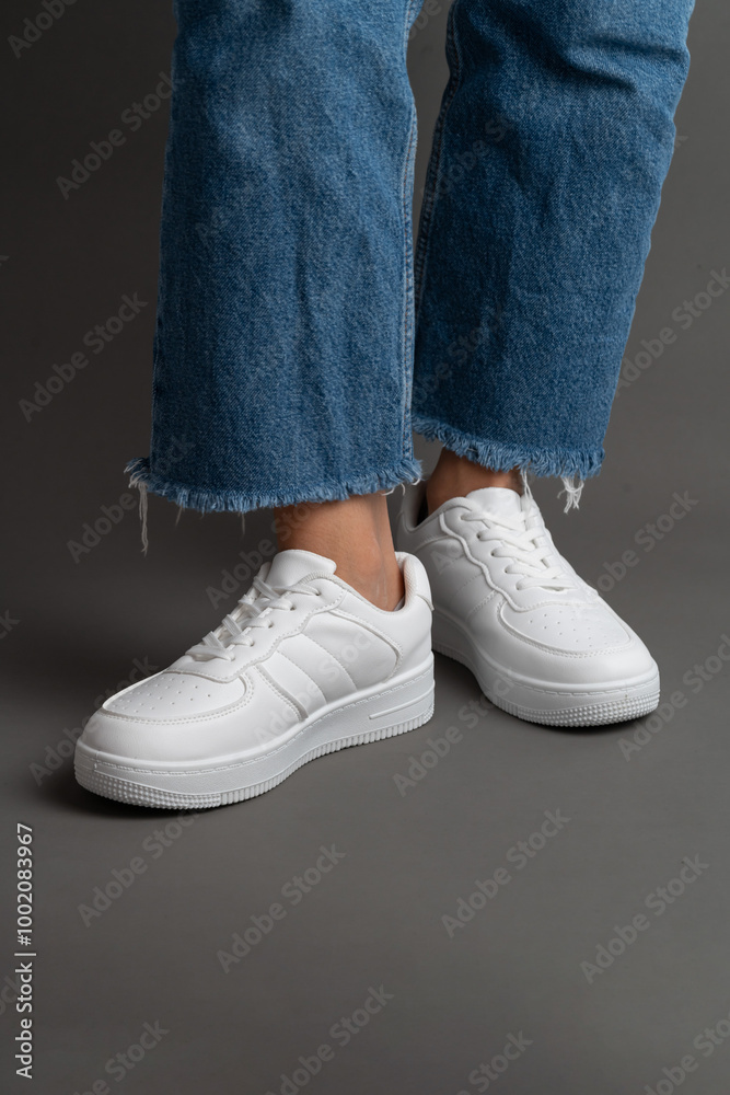 Woman's legs in white sneakers isolated on grey background Woman's legs in white sneakers isolated on grey background