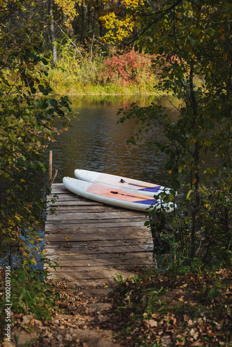 There are two paddle boards resting on a sturdy wooden dock that is located right next to a serene lake, creating a peaceful scene perfect for outdoor activities and relaxation