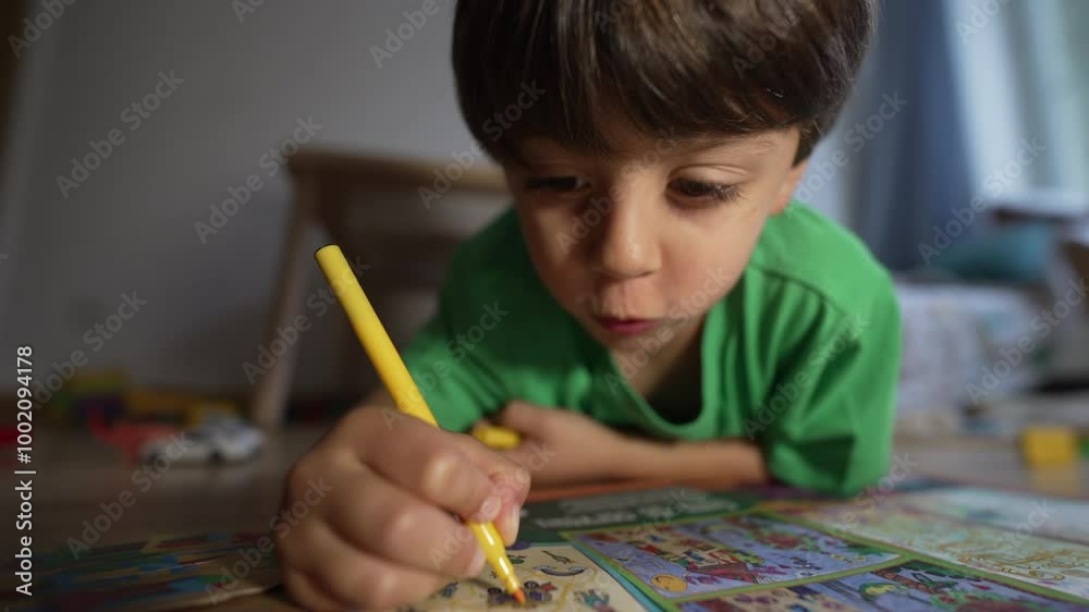 Young Boy Concentrated On Drawing With Yellow Marker, Lying On Floor In Comfortable Home, Green Shirt, Coloring Book, Creative And Educational Play, Indoors, Natural Light Young Boy Concentrated On Drawing With Yellow Marker, Lying On Floor In Comfortable Home, Green Shirt, Coloring Book, Creative And Educational Play, Indoors, Natural Light