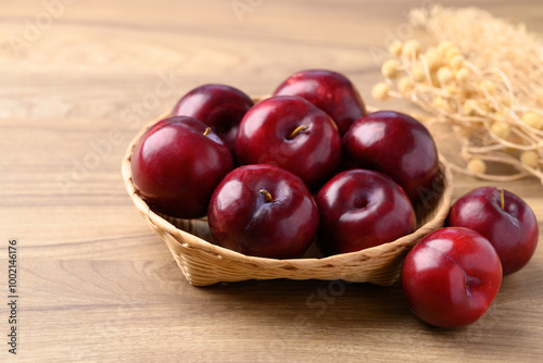 Red plum fruit in basket on wooden background