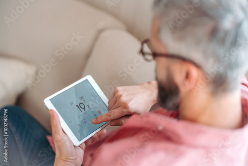 Man using smart thermostat, adjusting, lowering heating temperature at home. Concept of sustainable, efficient, and smart technology in home heating and thermostats.