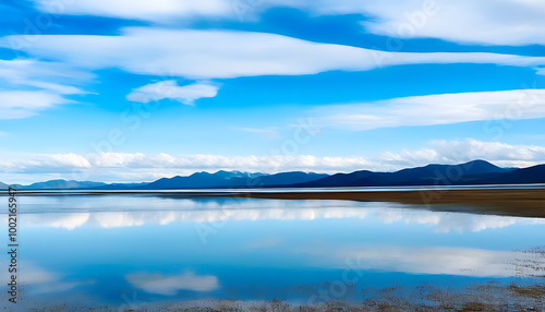 Wide lake reflects blue sky, mountains in sight.