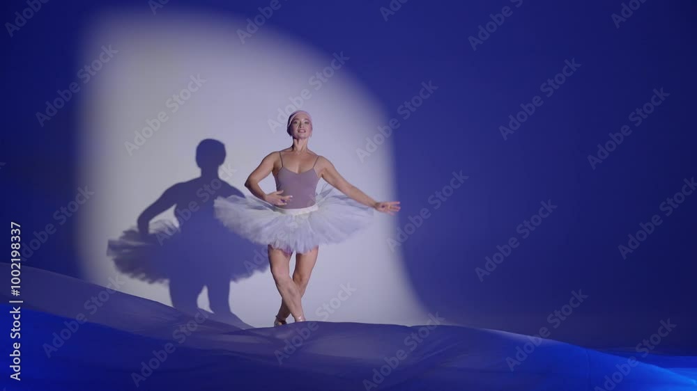 Graceful ballerina in a white tutu dance and perform dramatic choreographic elements on a white background, windy and beautiful dance, blue light and air fabric background, slow motion. Graceful ballerina in a white tutu dance and perform dramatic choreographic elements on a white background, windy and beautiful dance, blue light and air fabric background, slow motion.