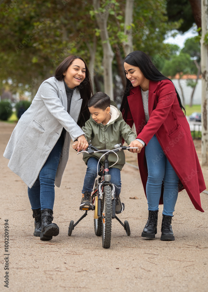Two young lesbian mothers helping their son learning to ride a bike in the park