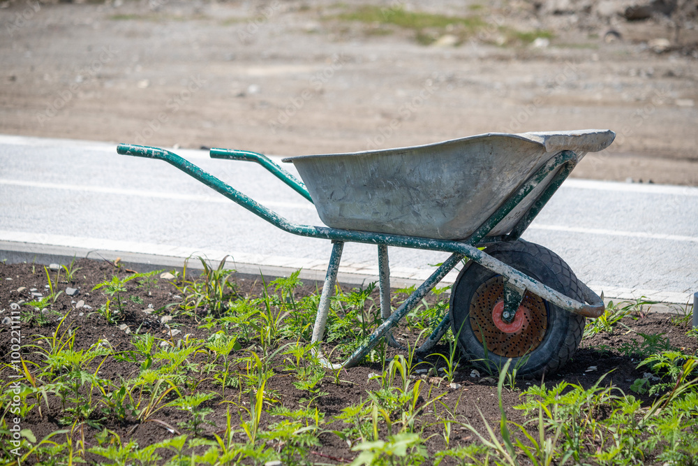 A wheelbarrow is sitting in the grass next to a road A wheelbarrow is sitting in the grass next to a road