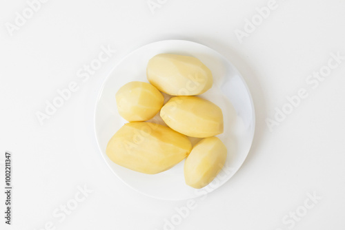 A white plate with five peeled potatoes, perfect for cooking holiday feasts or presenting vegetarian meal ingredients