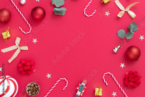 Frame of Christmas ornaments, candy canes, gifts, on red textured background.
