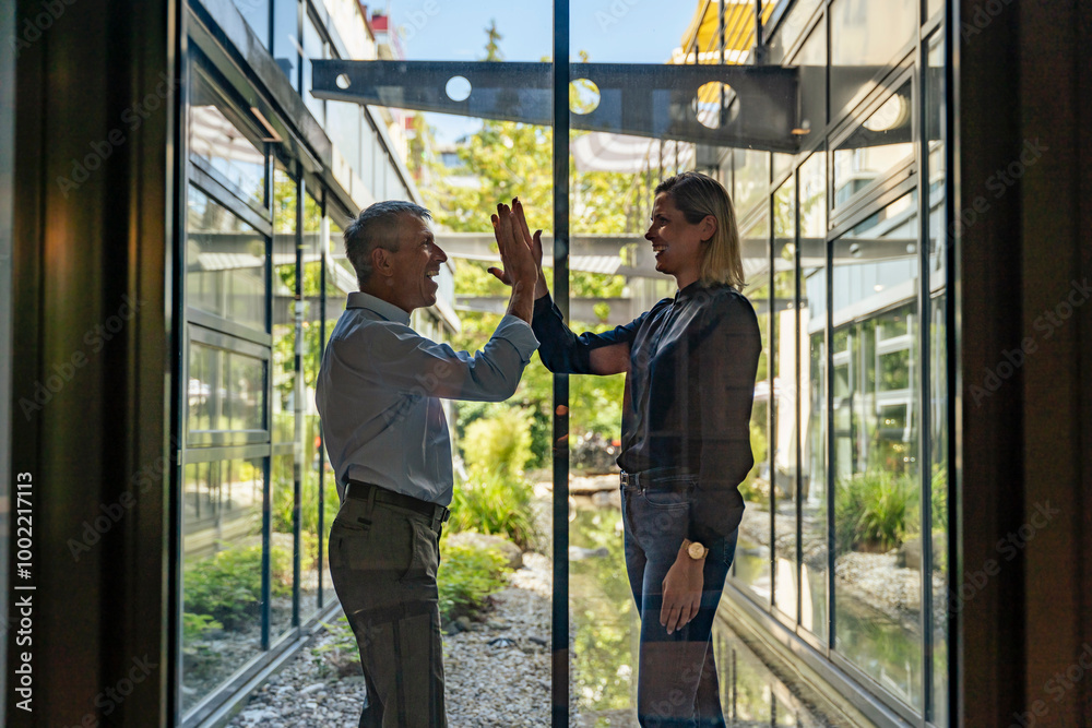 © Westend61 - Happy businessman giving high-five to businesswoman seen through glass © Westend61 - Happy businessman giving high-five to businesswoman seen through glass