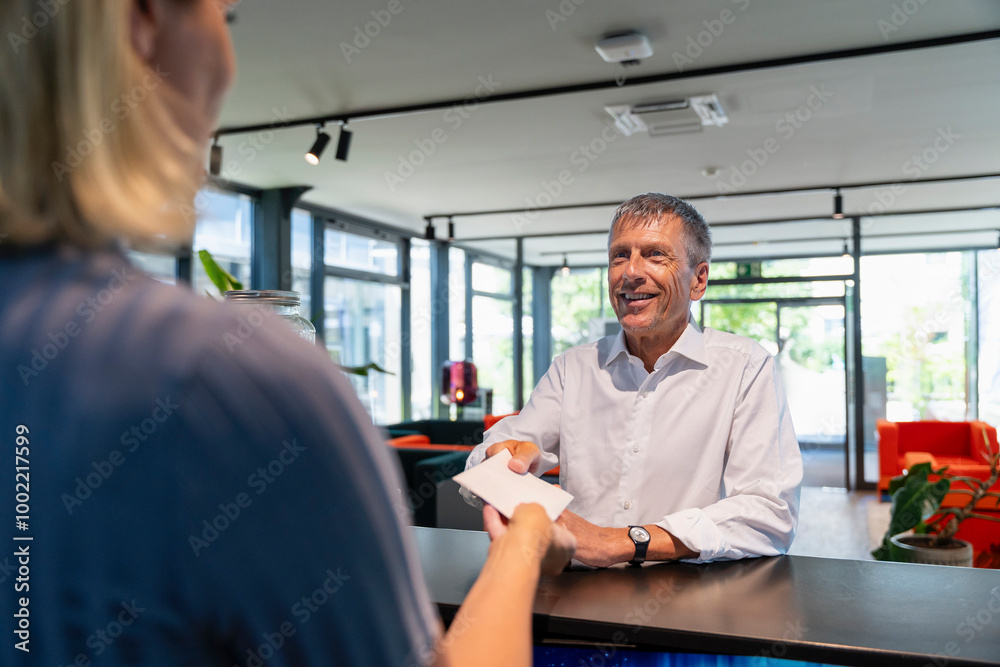 Receptionist giving letter to man at reception desk in hotel Receptionist giving letter to man at reception desk in hotel