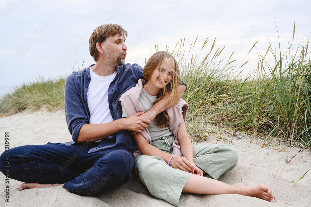 Playful father and daughter sitting on sand at beach Playful father and daughter sitting on sand at beach