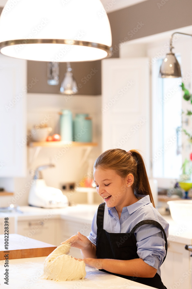Happy girl wearing apron kneading dough on kitchen counter at home Happy girl wearing apron kneading dough on kitchen counter at home