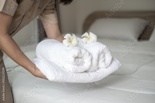 Hands of hotel maid putting plumeria flower and towels on the bed in the luxury hotel room ready for tourist travel