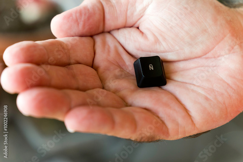 A hand holding a small black key with the spanish letter (N with a tilde) on it photo