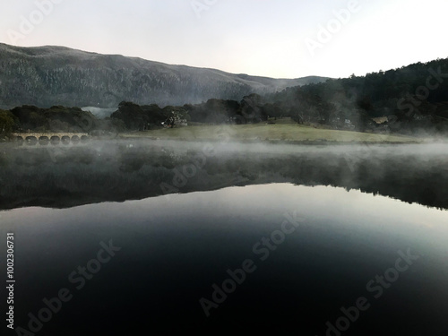 fog over the lake with the reflections of the mountains on the calm water photo