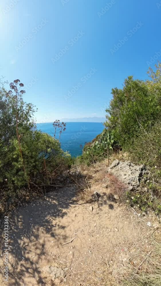 Vertical video. Wide-angle shot of a young couple walking along a coastal path, surrounded by vegetation, with the ocean visible to the side, capturing a peaceful outdoor stroll. Vertical video. Wide-angle shot of a young couple walking along a coastal path, surrounded by vegetation, with the ocean visible to the side, capturing a peaceful outdoor stroll.