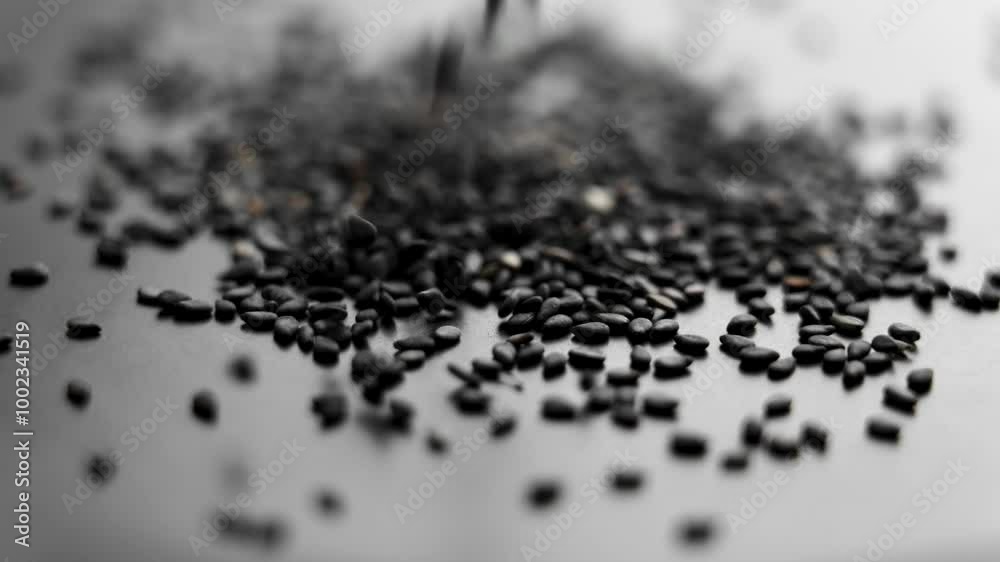 Dry organic sesame seeds falling on a black ceramic plate in slow motion. Uncooked scented spice. Macro shot. Dark view Dry organic sesame seeds falling on a black ceramic plate in slow motion. Uncooked scented spice. Macro shot. Dark view