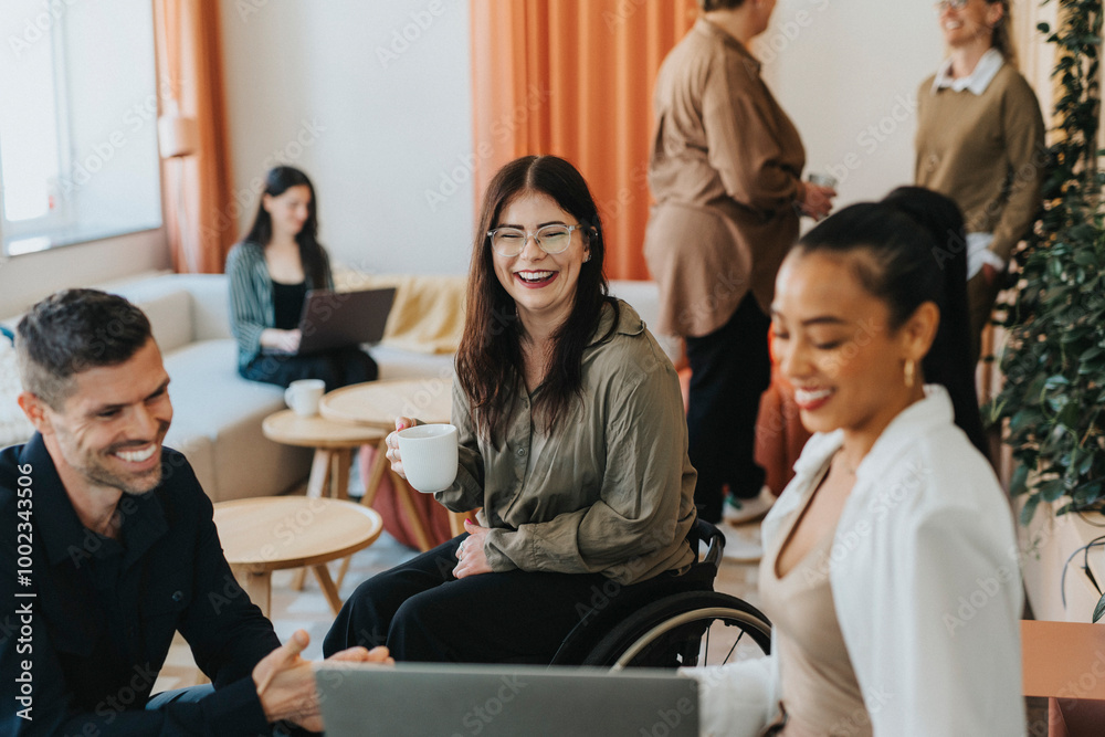 Happy female entrepreneur with physical disability discussing with colleagues at coffee break in office Happy female entrepreneur with physical disability discussing with colleagues at coffee break in office