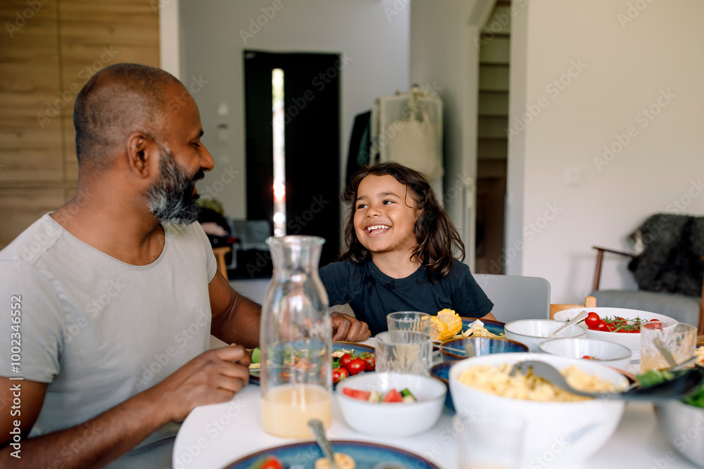 Happy boy having breakfast while sitting at dining table with father in home Happy boy having breakfast while sitting at dining table with father in home