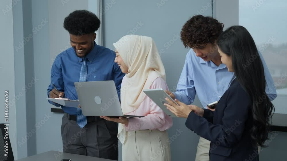 Joyful multicultural business team looks at a laptop together, sharing a moment of success in their modern office environment.
