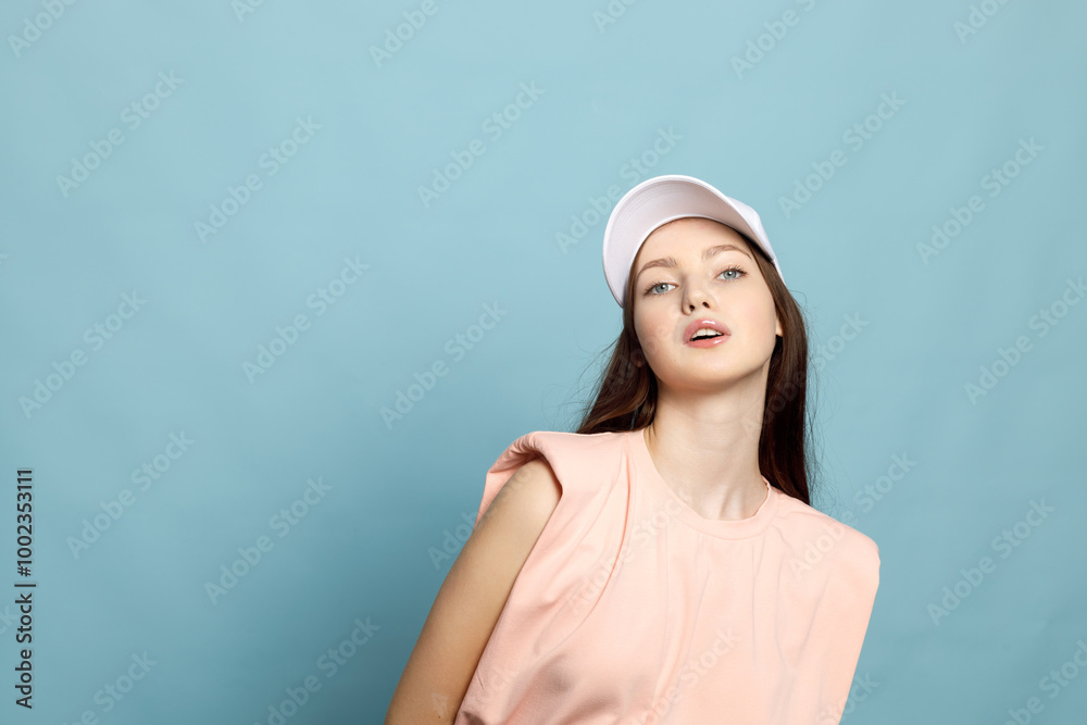Portrait of cheerful beautiful young woman wears cap, denim overalls and t shirt looks happy copy space isolated over blue background Portrait of cheerful beautiful young woman wears cap, denim overalls and t shirt looks happy copy space isolated over blue background