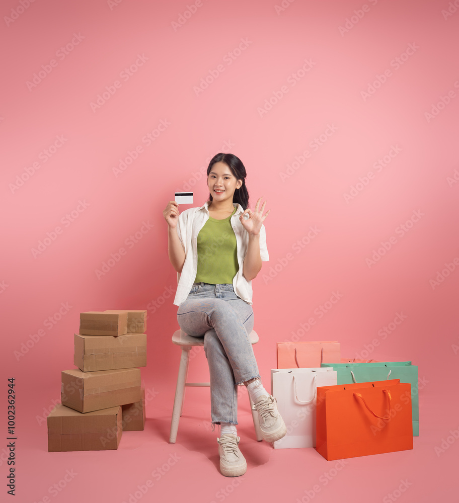 Portrait of Asian woman posing on pink background, next to shopping bags. Portrait of Asian woman posing on pink background, next to shopping bags.