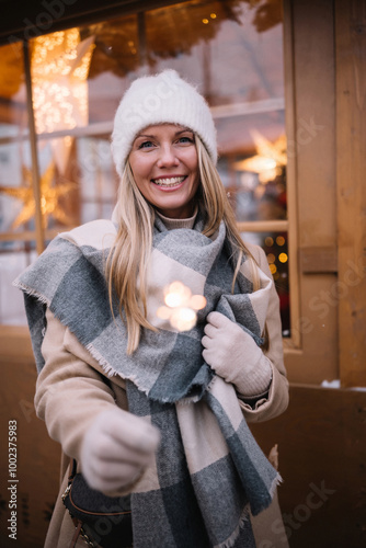 Portrait of young smiling woman holding sparkler in winter time outdoors.