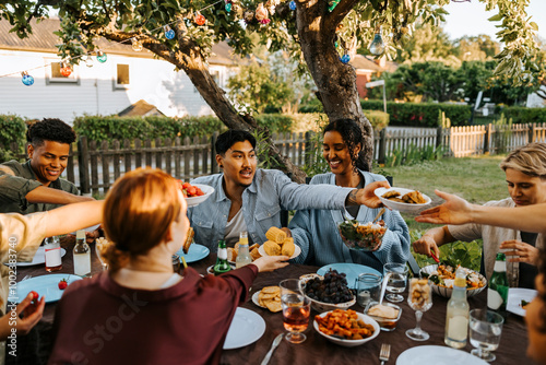 Male and female friends passing food to each other while having dinner in back yard at social gathering