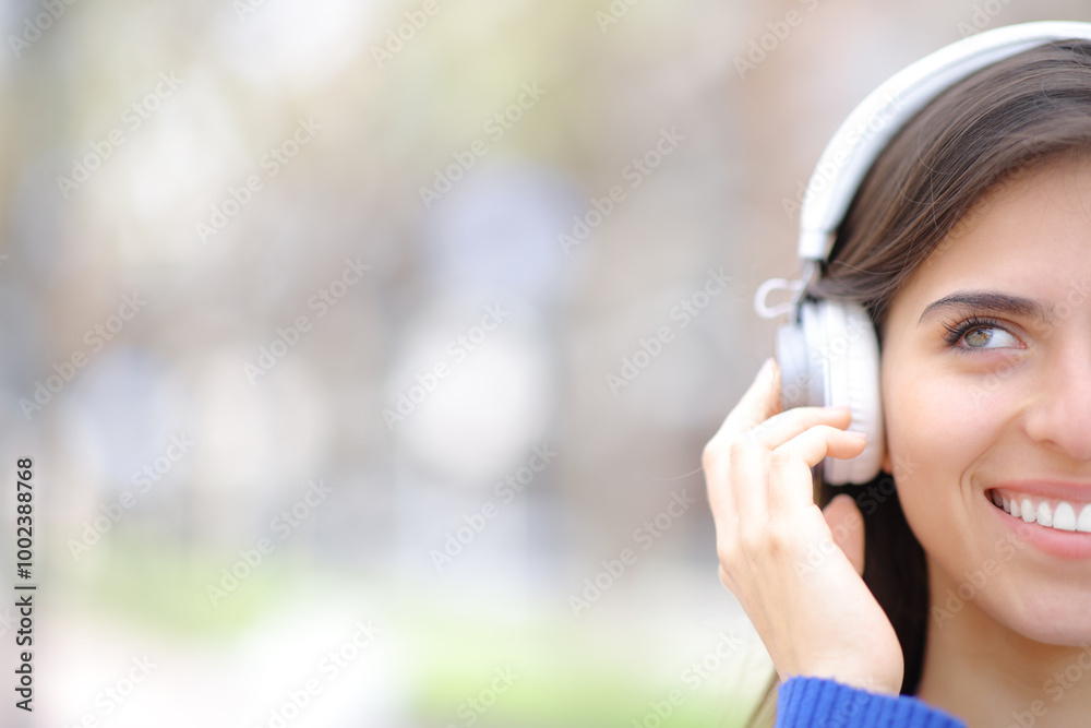 Half face of a happy woman looking at side wearing headphone Half face of a happy woman looking at side wearing headphone
