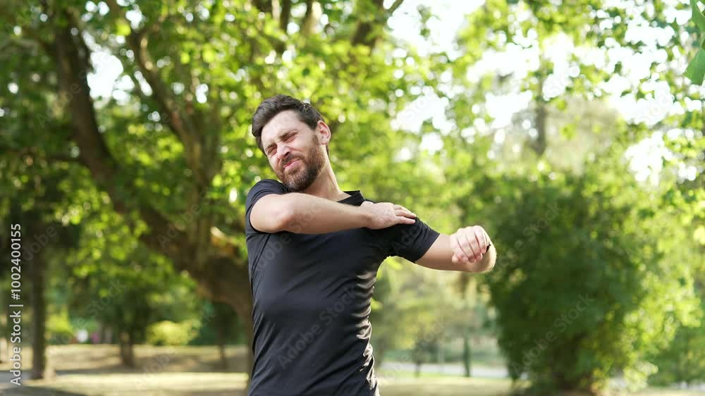 Adult athletic man experiencing acute shoulder pain during morning workout in urban city park. Upset male was injured. An unhappy athlete rubs and massages muscles on a sore spot, does hand exercises Adult athletic man experiencing acute shoulder pain during morning workout in urban city park. Upset male was injured. An unhappy athlete rubs and massages muscles on a sore spot, does hand exercises