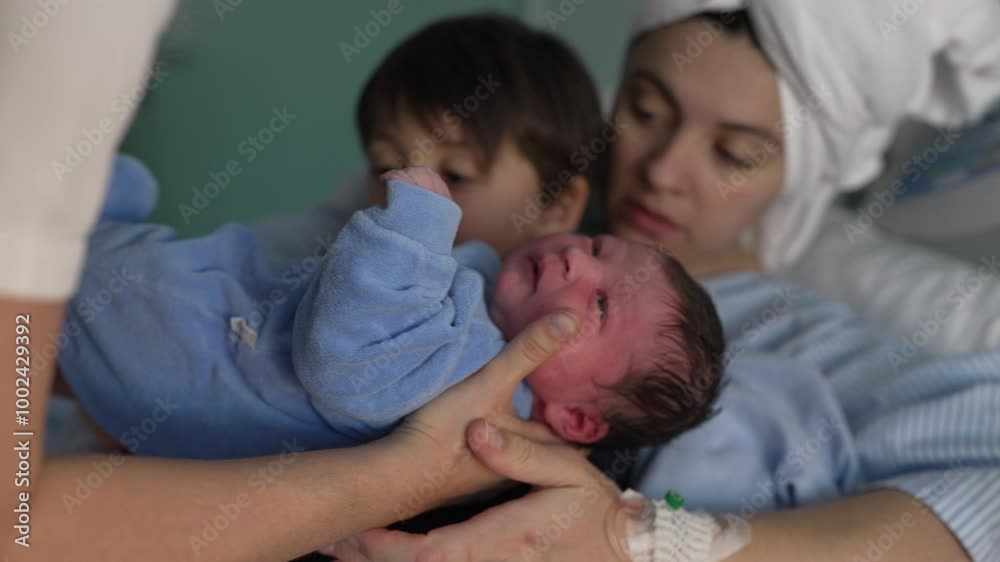 Mother and child welcoming newborn baby in arms at hospital after childbirth. nurse handing little infant to brother's arm next to mom at clinic, siblings bonding for the first time Mother and child welcoming newborn baby in arms at hospital after childbirth. nurse handing little infant to brother's arm next to mom at clinic, siblings bonding for the first time