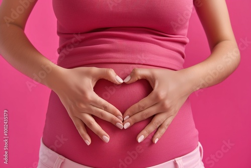 Female hand forming heart shape near woman belly on pink background. Close-up of healthy digestion concept. Woman abdominal area highlighted in pink, symbolizing balance and care for internal organs. photo