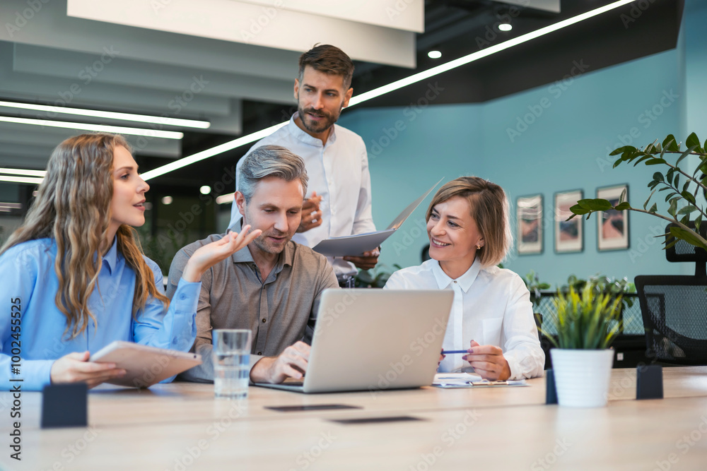 Fototapeta premium Four business professionals using laptop on desk discussing strategy company
