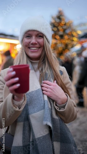 Young woman with long blonde hair cheers with hot drink at a festive outdoor market in winter
