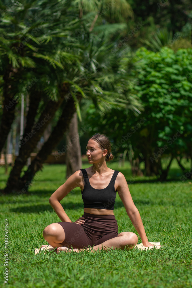 Young woman in sports clothes does yoga, smart fitness, Pilates, stretching on the lawn on a mat in the park. Concept of health, well-being. Vertical photo Young woman in sports clothes does yoga, smart fitness, Pilates, stretching on the lawn on a mat in the park. Concept of health, well-being. Vertical photo
