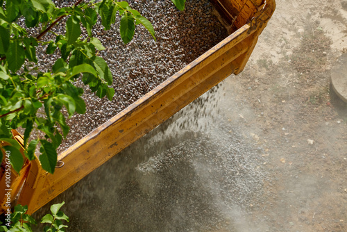 Construction gravel is being dumped from a truck bed at a construction site, close-up of gravel unloading.