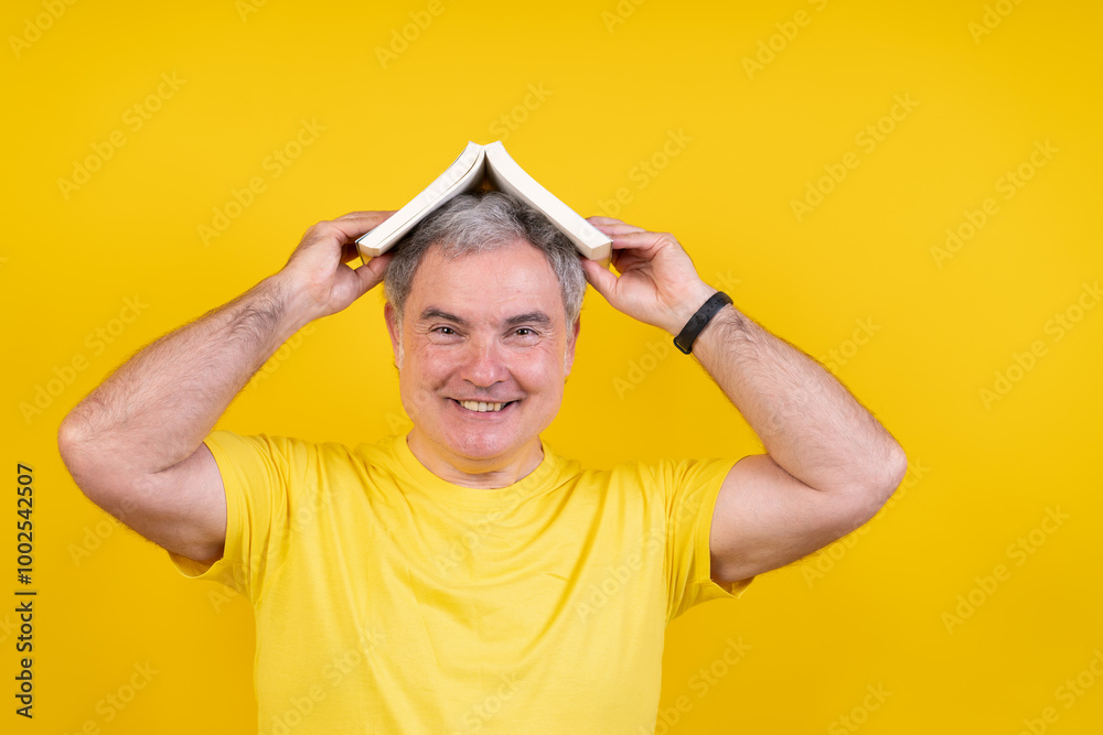 A man wearing a yellow shirt is holding a book on his head A man wearing a yellow shirt is holding a book on his head