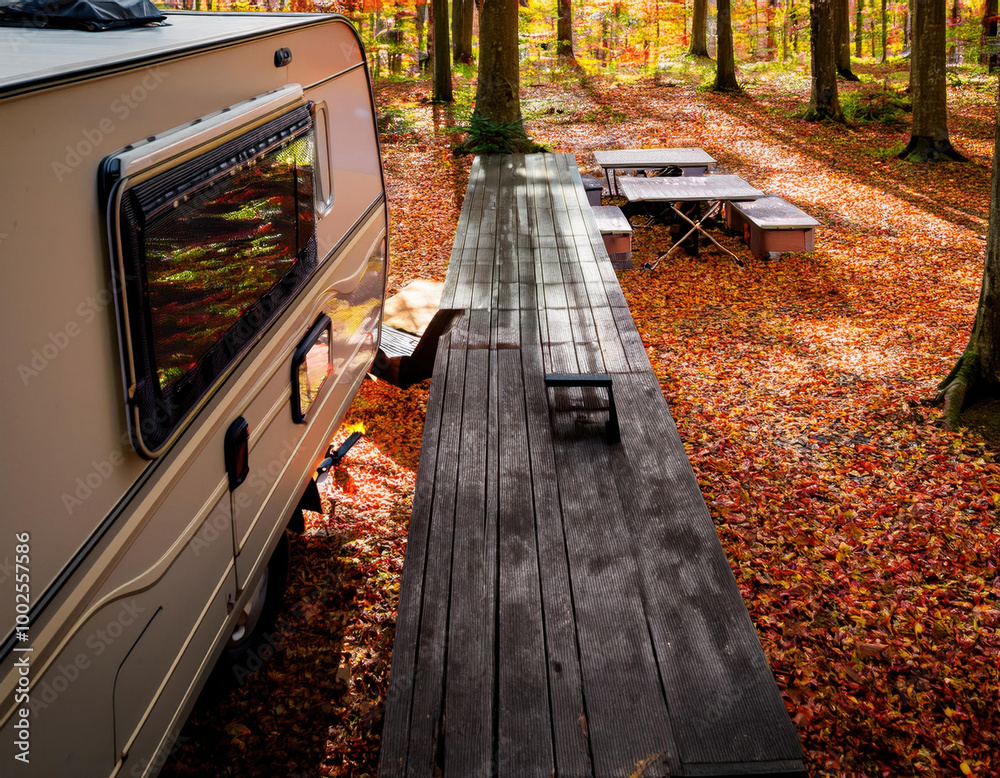 A cozy travel trailer parked amidst autumn foliage in a dense forest, featuring vibrant fallen leaves and soft sunlight filtering through the trees.