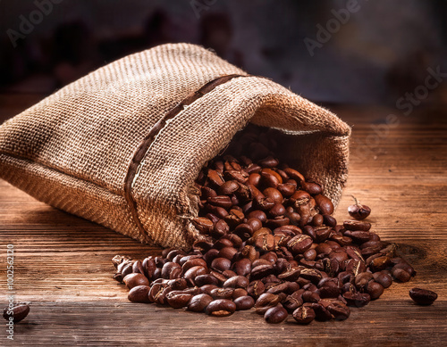 Obraz na płótnie A rustic burlap sack filled with roasted coffee beans spills onto a weathered wooden table, creating a warm and earthy visual that highlights the natural textures. w salonie