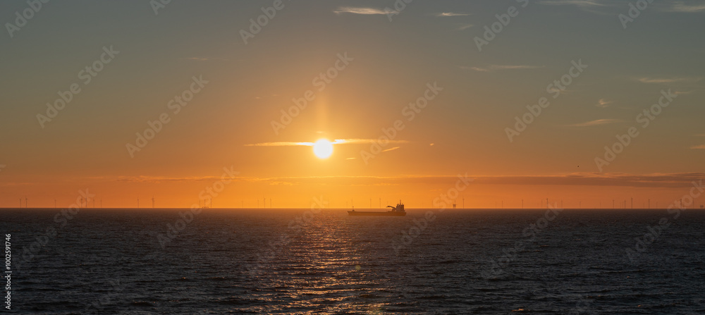 Panorama at sunset over the North Sea with a silhouette of a ship and a wind farm on the horizon. Panorama at sunset over the North Sea with a silhouette of a ship and a wind farm on the horizon.
