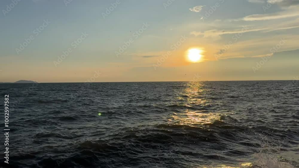 30 September 2024 Bang Saen Beach, Chonburi : A tranquil scene of a golden sunset over a vast, rippling ocean with a sliver of land in the distance. The sun is setting, casting a warm glow over the wa 30 September 2024 Bang Saen Beach, Chonburi : A tranquil scene of a golden sunset over a vast, rippling ocean with a sliver of land in the distance. The sun is setting, casting a warm glow over the wa