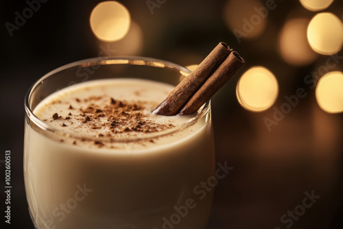 Glass of eggnog is garnished with cinnamon sticks and powdered cinnamon in front of holiday lights photo