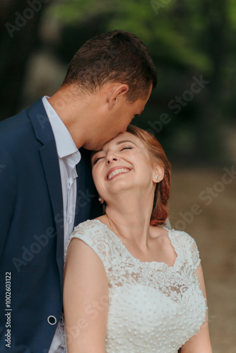 A bride and groom are kissing and hugging each other. The bride is wearing a white dress and the groom is wearing a blue suit. They are both smiling and seem to be happy