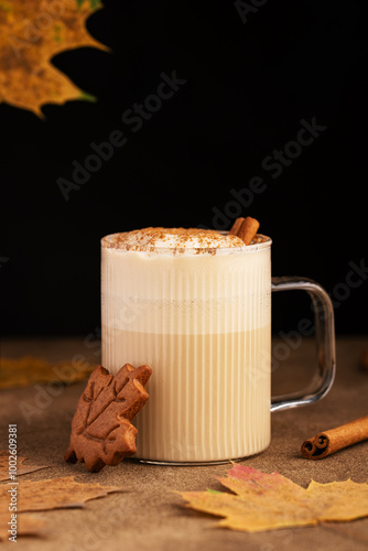 Autumn Raf coffee with espresso, maple syrup and whipped cream foam decorated ground cinnamon in a ribbed glass cup. Yellow maple leaves and cookie on background. Autumn still life. Space for text photo