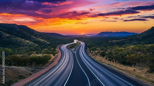 A multi-lane highway situated in the Australian outback, framed by colorful clouds and a vivid evening sky photo