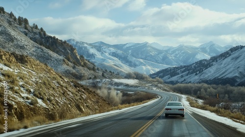 In winter, a white automobile travels through a mountain route that displays picturesque green mountains.