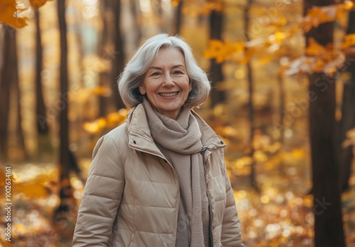 older woman in beige jacket smiling and walking in light autumn forest, lot of fallen leaves on ground