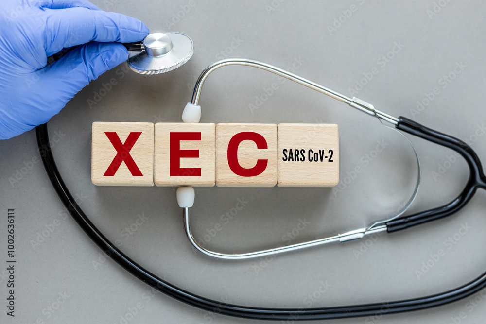 XEC, the latest subvariant of the SARS CoV-2 virus. The name of the Xec virus causing Covid-19 disease on wooden cubes. Stethoscope in doctor's hand, Medical concept, gray background, flat lay