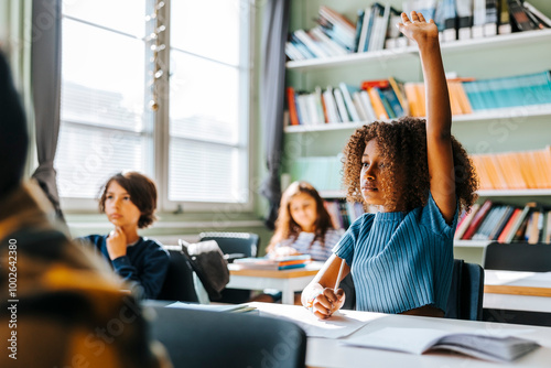 Curly hair girl with hand raised sitting in classroom at school photo