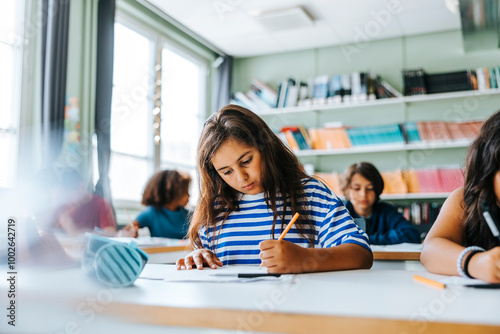 Focused girl with long hair giving exam while sitting in classroom at elementary school